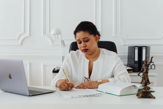 African American woman lawyer signing documents at a desk, symbolizing professionalism. Markedsføringsloven: hvor finder du de officielle kilder?